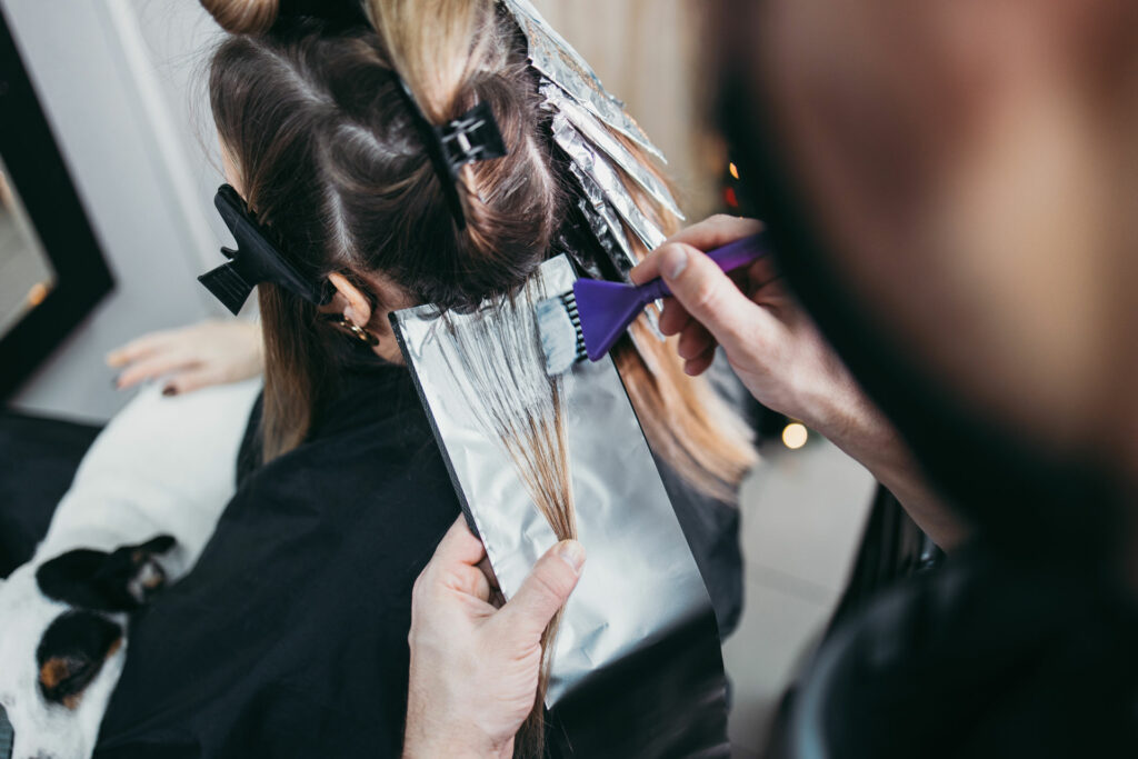 Hairdresser is dyeing female hair, making hair highlights to his